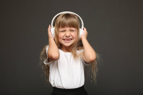 дитяча дівчина насолоджується музикою у великих білих навушниках і посмішкою. Сині очі блондинка волосся дівчина слухати музику
 - Фото, зображення