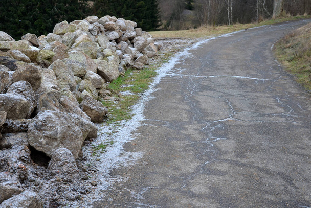pile of granite stones in a landfill by the road. Asphalt frozen road in the countryside near a pile of cobblestones gray ready for construction of a retaining wall in the garden - Photo, Image