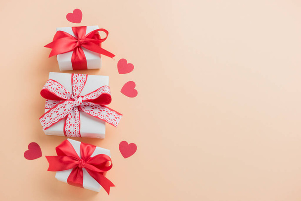 Confezioni regalo con nastro rosso e cuori su sfondo beige pastello. Composizione di San Valentino con spazio libero. Vista dall'alto, piatta - Foto, immagini