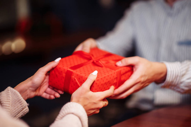 Valentine's Day concept. Close shot of man's and woman's hands presenting gifts to each other at a cafe. A young loving couple celebrating in the restaurant. New normal, winter holidays - Photo, Image