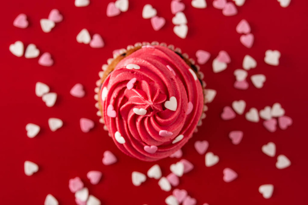 Cupcake διακοσμημένο με καρδιές ζάχαρης για την Ημέρα του Αγίου Βαλεντίνου σε κόκκινο φόντο. Άνω όψη - Φωτογραφία, εικόνα