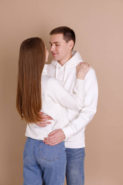 恋人のカップルは、バレンタインデーにベージュの背景に抱きしめます - 写真・画像
