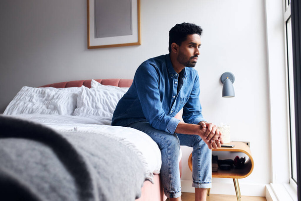 Onneton nuori mies mielenterveysasioissa istuu sängyn reunalla - Valokuva, kuva