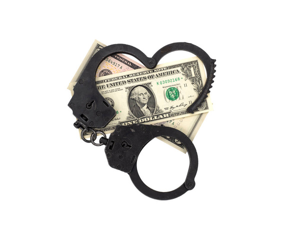 Bir dolarlık banknotların üzerinde kalp şeklinde polis kelepçeleri aç. Beyaz arka planda izole edilmiş bir fotoğraf. Rüşvet, mali suç, hükümet yolsuzluğu kavramı. - Fotoğraf, Görsel