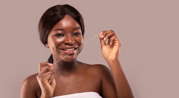 Στοματική υγιεινή. Ελκυστική Αφρικανή γυναίκα που χρησιμοποιεί οδοντικό νήμα και χαμογελώντας στην κάμερα - Φωτογραφία, εικόνα