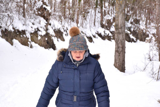 Mulher aposentada de casaco e chapéu com cores brilhantes olhando onde ela pisa em um caminho cheio de neve na floresta. Cena após a tempestade de neve chamada Filomena em Espanha. Janeiro de 2021. - Foto, Imagem