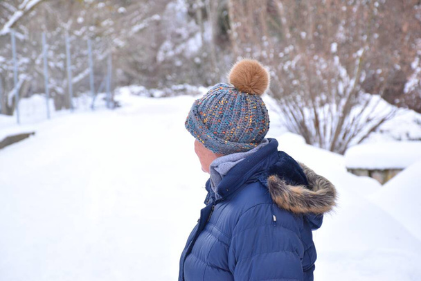 Πλάγια άποψη της μεγαλύτερης γυναίκας στο σακάκι και καπέλο με πολύχρωμες ρίγες απολαμβάνοντας το χιόνι. Σκηνή μετά τη χιονοθύελλα που ονομάζεται Φιλομίνα στην Ισπανία. Ιανουάριος 2021. - Φωτογραφία, εικόνα