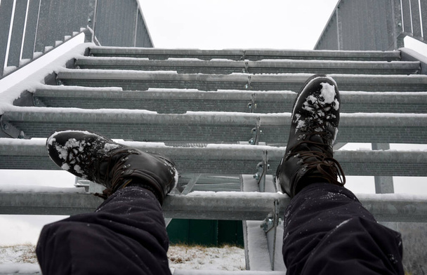 Widok turystyczny z metalowych schodów niebezpiecznie ślizga się zimą. Turysta w butach wypadł ze skóry i leżał ranny na schodach. połamane nogi z siniakami, niebezpieczeństwo upadku. złamanie, kość, kości - Zdjęcie, obraz