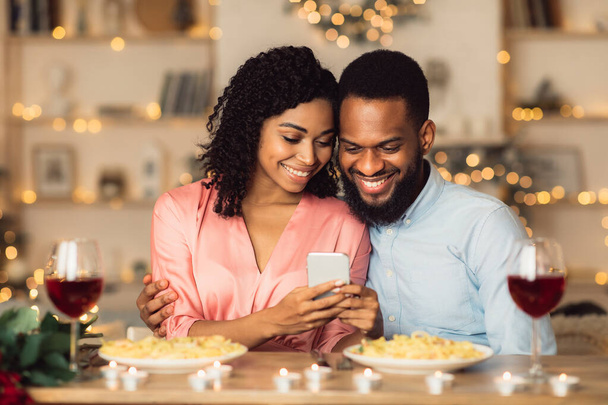 Glimlachende zwarte man en vrouw met smartphone tijdens het diner - Foto, afbeelding