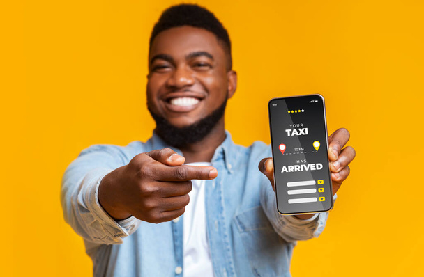 Chico negro alegre señalando en el teléfono inteligente con la aplicación de tarifa de taxi abierto - Foto, imagen
