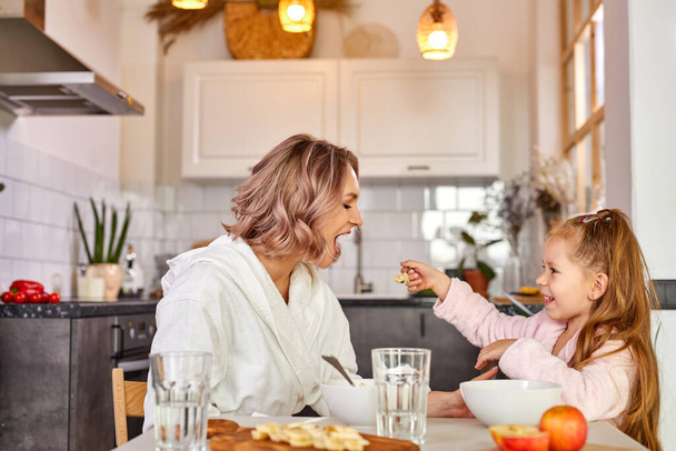 madre feliz con niña comiendo sabrosa papilla para el desayuno - Foto, Imagen