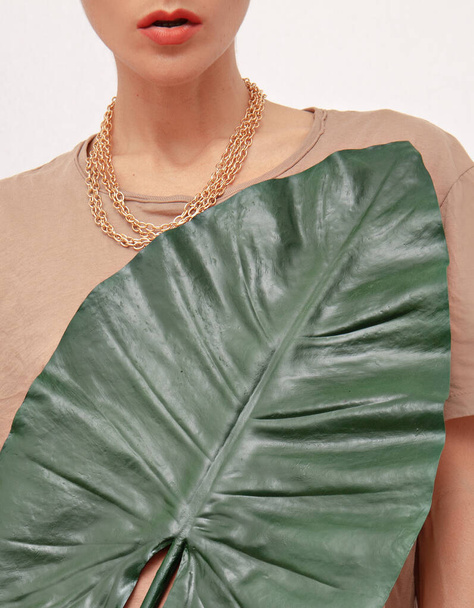 Неузнаваемая женская модель в повседневной комфортной бежевой рубашке из хлопка и ювелирных украшениях с пальмовым листом. Весной свежая концепция экологического био-стиля - Фото, изображение