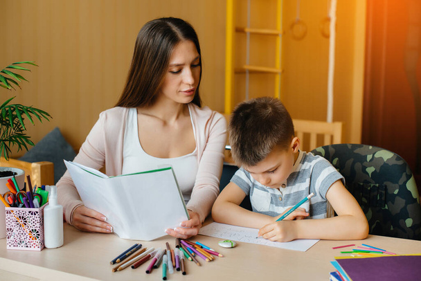 A young mother is doing homework with her son at home. Parents and training - Zdjęcie, obraz