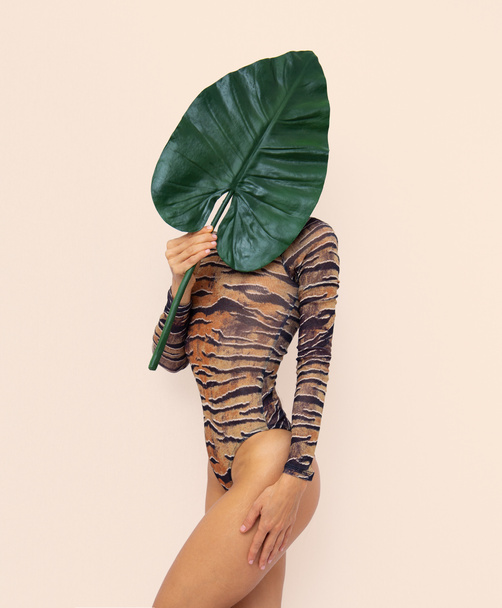 ファッション虎のボディスーツにヤシの葉を保持認識できない女性。熱帯ジャングル野生の創造的な概念。エコミニマリストファッションの詳細 - 写真・画像