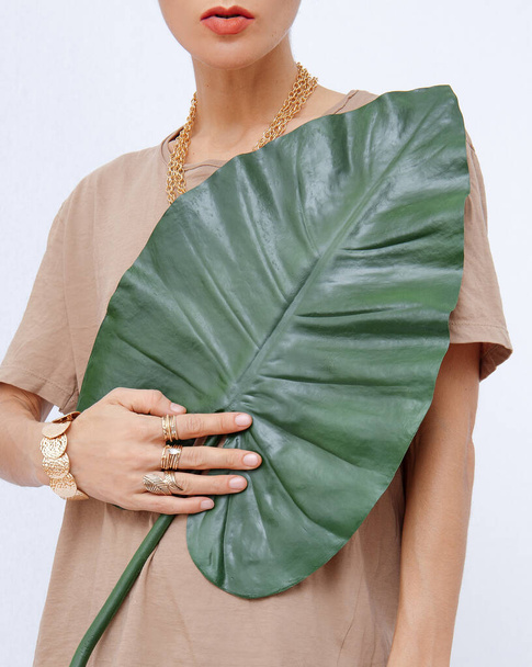 Unrecognizable female model in casual comfort beige monochrome cotton t-shirt and jewelry with palm leaf. Spring summer fresh eco bio style concept - Photo, Image