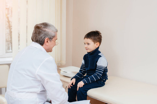 A young boy is listened to and treated by an experienced doctor in a modern clinic. A virus, and an epidemic - Foto, immagini