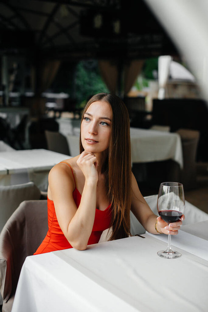 Beautiful young girl sits and drinks wine on the veranda of a beautiful house. Holiday. - Foto, immagini