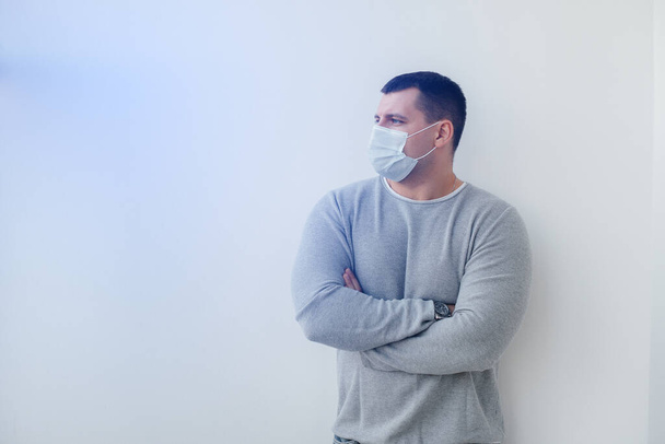 A young man stands on a gray background wearing a mask during a quarantine with free space. Quarantine in the mask - Foto, Imagem