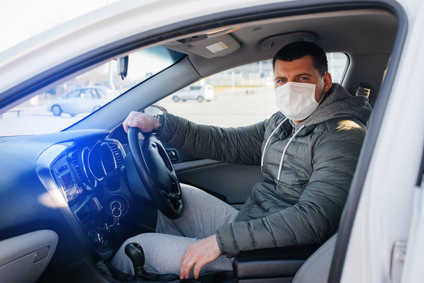 A young man sits behind the wheel wearing a mask for personal safety while driving during a pandemic and coronavirus. Epidemic - Foto, Imagem