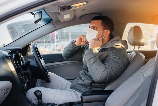A young man sits behind the wheel wearing a mask for personal safety while driving during a pandemic and coronavirus. Epidemic - Foto, Bild