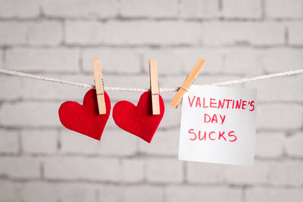 Red hearts and note "Valentine's day sucks" hanging on clothespins. Hate of Valentine's day concept. - Foto, afbeelding