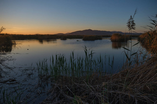 вид на спокойную воду в озере на закате в далеких горах - Фото, изображение
