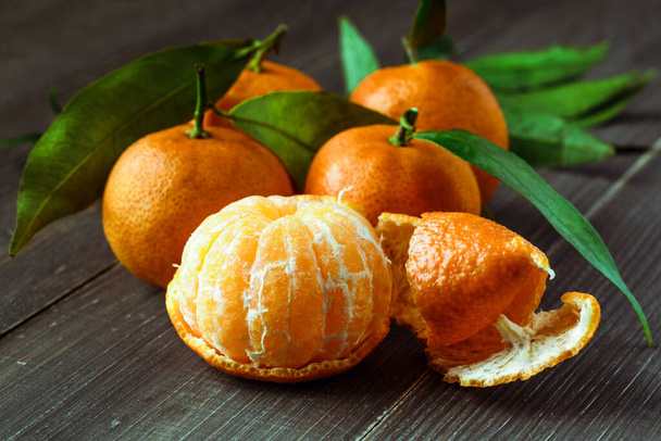 Ripe Mandarin fruit peeled open and place on old rustic look timber with group of mandarin fruits and leaves out of focus on the background - Foto, afbeelding