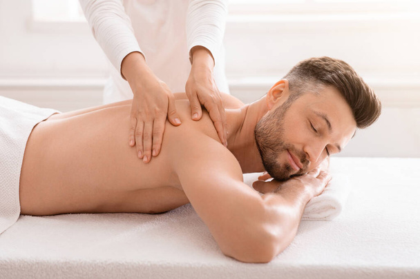 Terapeuta feminino esfregando alegre homem ombros no salão de spa - Foto, Imagem