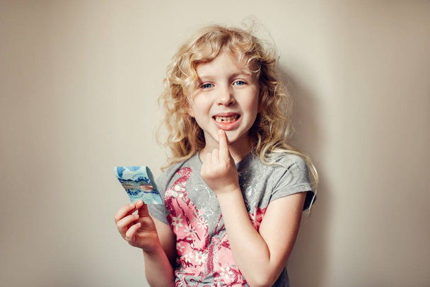 Kaukasische blonde Mädchen zeigt ihren fehlenden Zahn im Mund und hält Geld von Zahnfee. Stolzes Kind, das verlorenen Zahn zeigt. Aufwachsen und Adoleszenz.  - Foto, Bild