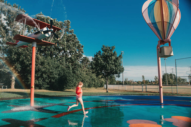 Nettes entzückendes kaukasisches lustiges Mädchen, das an einem Sommertag auf dem Spritzpolsterspielplatz spielt. Saisonale Wassersportaktivitäten für Kinder im Freien.  - Foto, Bild