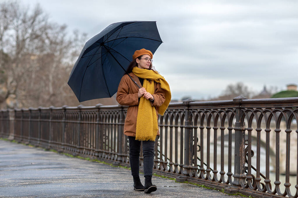 Dziewczyna z parasolem spaceruje po mieście. Młoda kobieta w zimowej sukience i parasolce, chodzi w chłodny zimowy dzień. - Zdjęcie, obraz