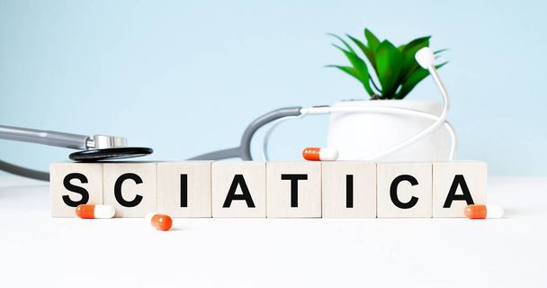 SCIATICAという言葉は木製の背景に聴診器の近くの木製の立方体に書かれています。医学的概念 - 写真・画像