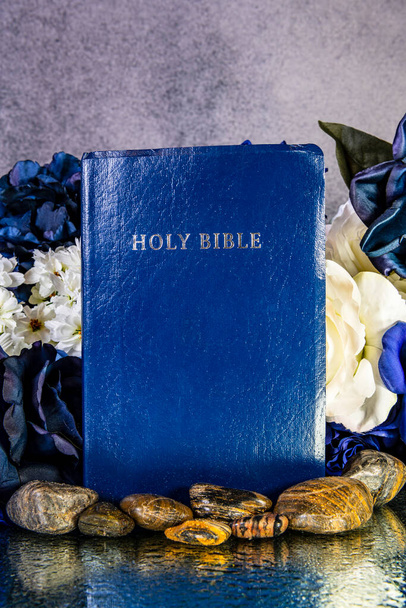 μπλε Βίβλος που περιβάλλεται από πέτρες και λουλούδια αντανακλώντας σε υγρό καθρέφτη - Φωτογραφία, εικόνα