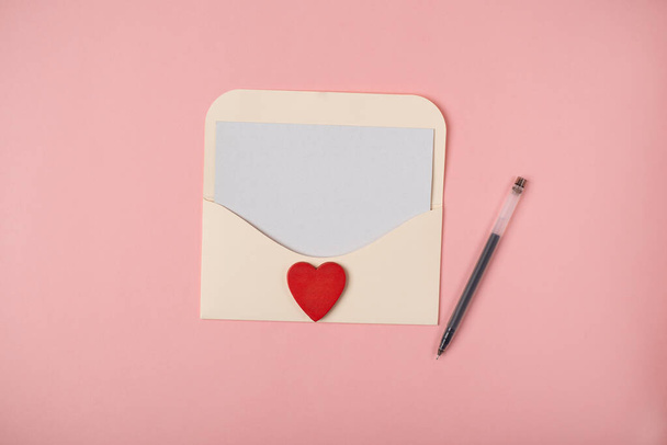 Busta con un foglio bianco di carta all'interno e cuore rosso sullo sfondo rosa. Lettera d'amore romantica per il concetto di San Valentino. Spazio per testo. - Foto, immagini