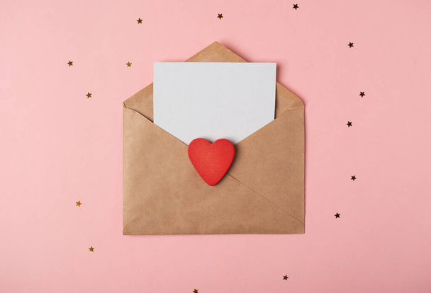Craft envelope with a blank sheet of paper inside and red heart on the rose background. Romantic love letter for the Valentine's day concept. Space for text. - Photo, Image