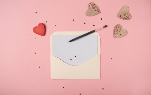 Craft envelope with a blank sheet of paper inside and red wooden heart on the rose background. Romantic love letter for the Valentine's day concept. Space for text. - Foto, afbeelding