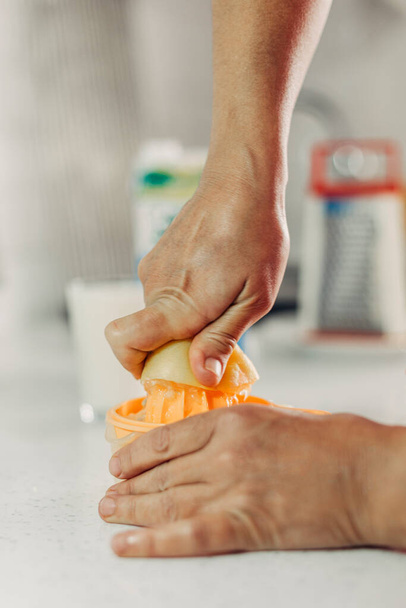 Πιέστε το λεμόνι στο χέρι με τον αποχυμωτή λεμονιού στην κουζίνα - Φωτογραφία, εικόνα
