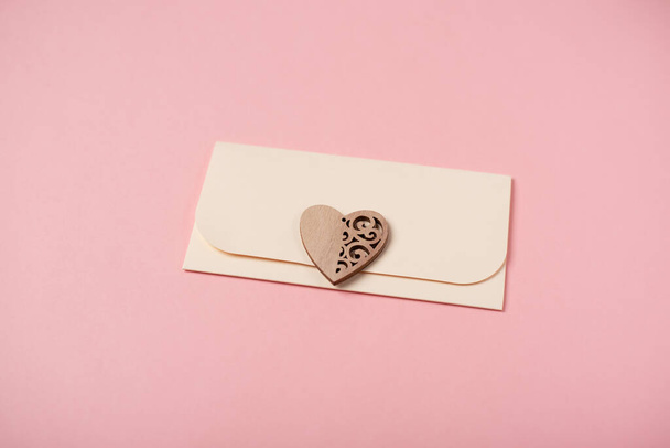 Envelope and wooden heart on the rose background. Flat lay. Romantic love letter for Valentine's day concept. - Фото, изображение