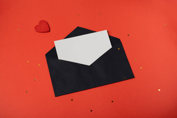Black envelope with a blank sheet of paper inside and red heart on the red background. Romantic love letter for the Valentine's day concept. Space for text. - Fotoğraf, Görsel