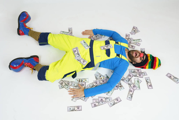 Humor and fun concept. A clown in a bright suit lies on the floor, his money is around - Valokuva, kuva