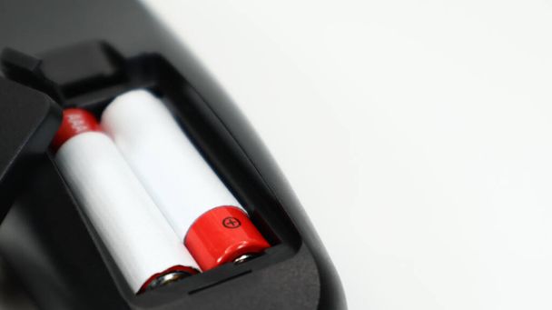 Schwarze TV-Fernbedienung mit AAA-Alkaline-Batterien in rot und weiß auf weißem Hintergrund. Batteriewechsel, Ersatzteile. Fernbedienung Batteriefach aus nächster Nähe. Kopierraum - Foto, Bild