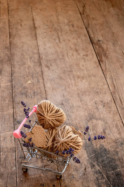 mini shopping cart filled with do it yourself jute hearts and lavender flowers on wooden background. zero waste Valentine's Day concep - Zdjęcie, obraz