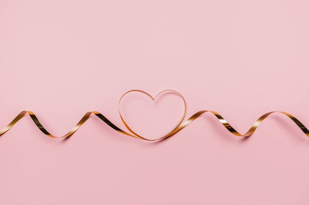 shape heart by gold ribbon on isolated pink background - Foto, imagen