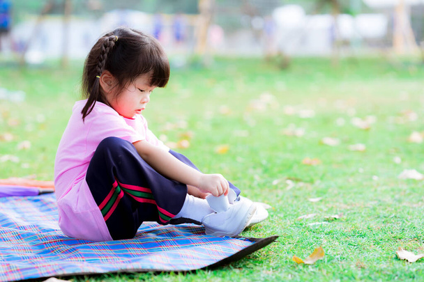 Активная милая девушка пытается носить кроссовки для спорта на газоне. Дети практикуют основные повседневные занятия. Счастливый ребенок носит спортивные штаны. Детям 3-4 года. - Фото, изображение