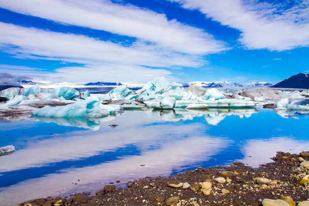 Iceland. Clouds reflected in the smooth water of the largest glacial lagoon Jokulsaurloun. White and blue icebergs and ice floes. Cold early summer morning. The concept of northern and photo tourism - Photo, image