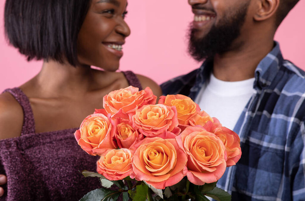 Ζευγάρι των sweethearts κρατώντας όμορφο μπουκέτο τριαντάφυλλα για την Ημέρα του Αγίου Βαλεντίνου πάνω από ροζ φόντο στούντιο, επιλεκτική εστίαση - Φωτογραφία, εικόνα
