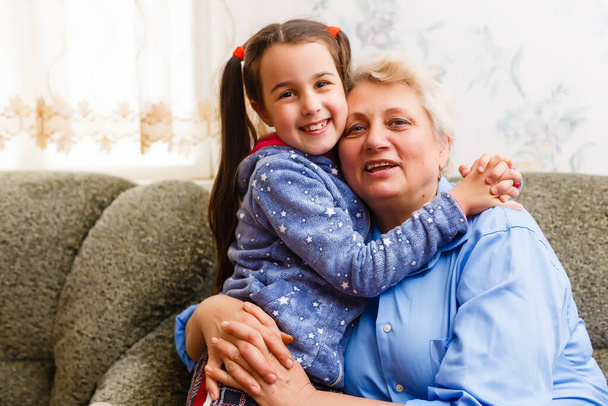Malá roztomilá holčička a její babička spolu tráví čas doma. Bavit se, objímat a usmívat, zatímco sedí na pohovce. - Fotografie, Obrázek