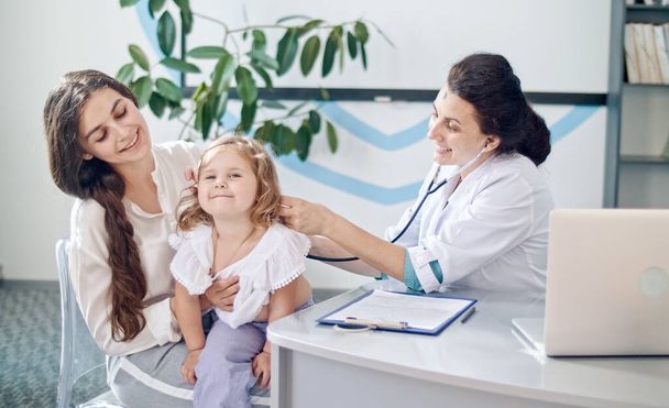Ärztin Kinderärztin mit Stethoskop Hören Sie das Herz eines glücklichen gesunden süßen Mädchens bei einem Arztbesuch mit Mutter im Krankenhaus. Ärztin untersucht Kind. - Foto, Bild