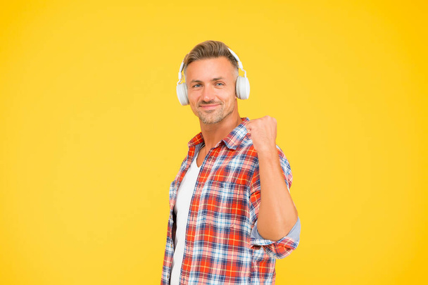 Happy man clench fist listening to music playing in modern earphones yellow background, audio - Valokuva, kuva