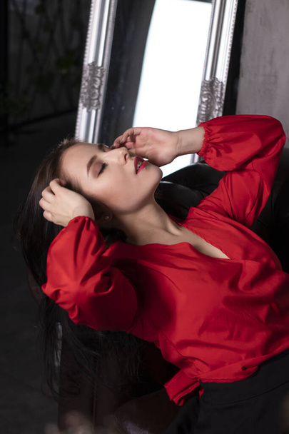 retrato de mujer morena atractiva en blusa roja acostada en sofá de cuero. San Valentín. espacio de copia. - Foto, imagen